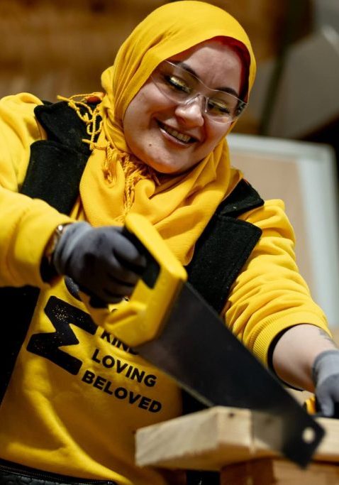 A woman holds a saw, cutting a piece of wood.