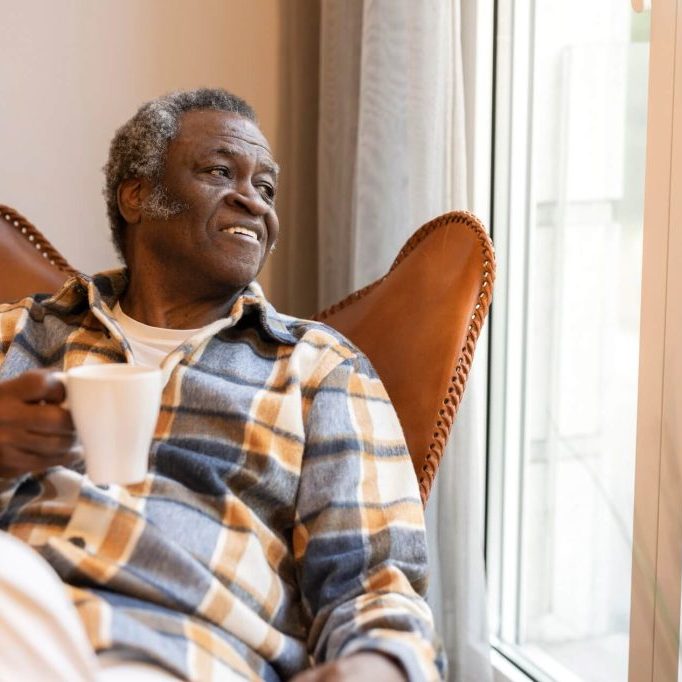 A man sits comfortably on a chair, holding a cup in his hand.